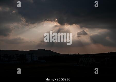 Raggi di luce solare che si infrangono attraverso nuvole pesanti su paesaggi silhouette di Cipro sud-orientale. Foto Stock