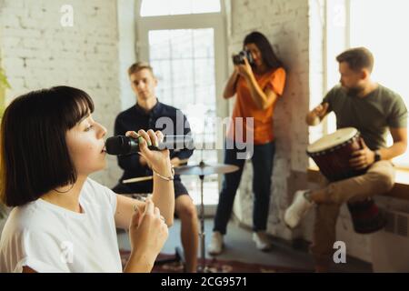 Sessione. Band musicista jamming insieme in un posto di lavoro d'arte con strumenti. Uomini e donne caucasici, musicisti, suonando e cantando insieme. Concetto di musica, hobby, emozioni, occupazione artistica. Foto Stock