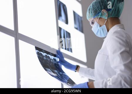 Medico in maschera medica protettiva e guanti esamina un radiografia. Foto Stock
