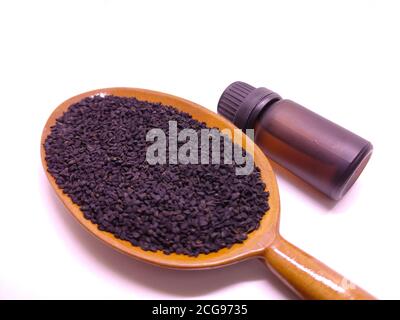 Bottiglia di vetro di olio essenziale di semi di cumino nero, Nigella Sativa in cucchiaio di legno su fondo bianco. Concetto di medicina di erbe Foto Stock