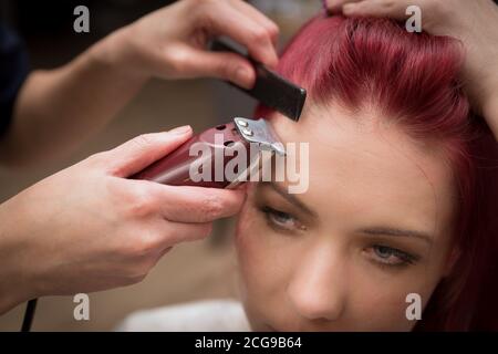 Le mani del parrucchiere accorciano i capelli della ragazza per creare un'acconciatura elegante. Foto Stock