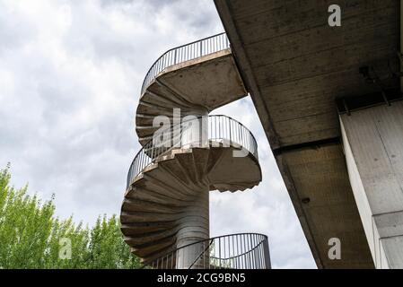 Scala a chiocciola in cemento con corrimano in metallo per il traffico pedonale fino al ponte. Foto Stock