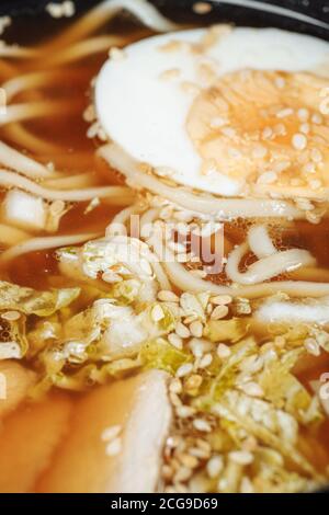 Zuppa di noodle asiatica, ramen con pollo, tofu, verdure e uova in ciotola nera. Sfondo ardesia Foto Stock