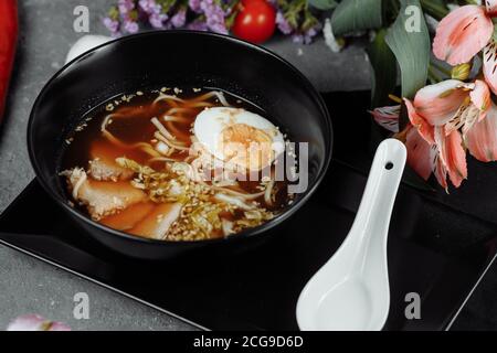 Zuppa di noodle asiatica, ramen con pollo, tofu, verdure e uova in ciotola nera. Sfondo ardesia Foto Stock