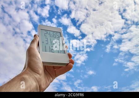 Migliore stazione meteo personale con condizioni meteorologiche interne ed esterne. Un uomo tiene un gadget in mano su uno sfondo di cielo e nuvole Foto Stock