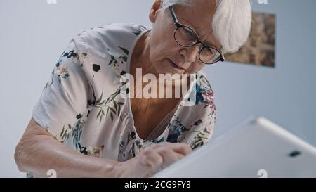 Donna anziana con capelli grigi e occhialse che usa il tabet. Scatto ad angolo basso. Foto di alta qualità Foto Stock