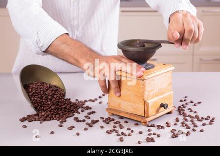 Uomo caucasico in abiti bianchi macinando il caffè con i fagioli rovesciati sopra il tavolo Foto Stock