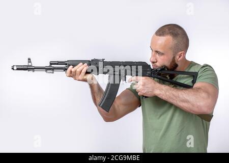Forte sparatutto caucasico in abbigliamento casual con fucile da cecchino in piedi in posizione che mira da parte isolato su bianco Foto Stock
