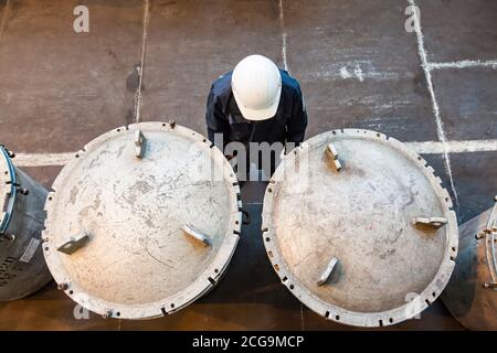 Impianto di metallurgia del titanio. Vasca di stoccaggio in metallo per aste in metallo di titanio. Ingegnere in cappello bianco. Foto Stock