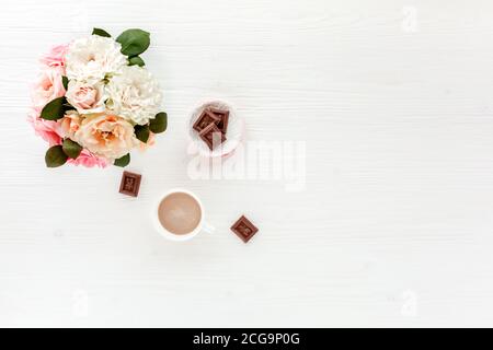 Spazio di lavoro femminile con fiori rosa e beige rose, accessori, diario su sfondo bianco. Disposizione piatta, vista dall'alto, stile alla moda e sfondo femminile. Foto Stock