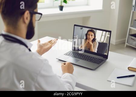 Consultazione medica online. Un uomo seduto nel suo ufficio usa un laptop, una videochiamata e ascolta un paziente. Foto Stock