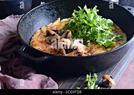 Frittata con patate, funghi, rucola ed erbe per colazione su fondo scuro. Foto Stock