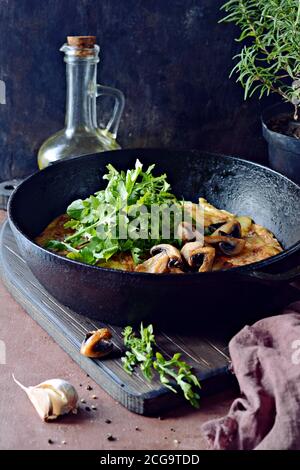 Frittata con patate, funghi, rucola ed erbe per colazione su fondo scuro. Foto Stock