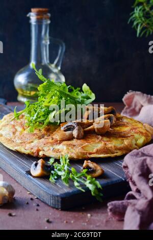 Frittata con patate, funghi, rucola ed erbe per colazione su fondo scuro. Foto Stock