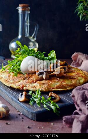 Frittata con patate, funghi, rucola ed erbe per colazione su fondo scuro. Foto Stock