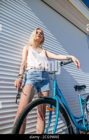 Bella ragazza con capelli biondi felicemente a cavallo bicicletta. Ritratto  di giovane donna in jeans e occhiali da sole sulla testa divertendosi  mentre cavalcando sulla bicicletta rossa A Foto stock - Alamy
