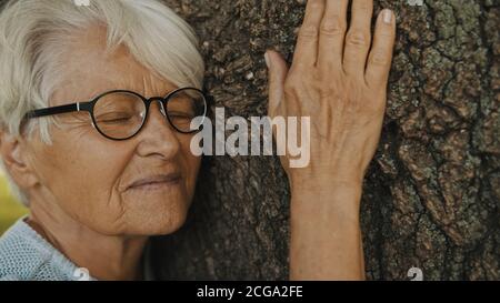 Ritratto di donna alta con capelli grigi che abbracciano l'albero. Foto di alta qualità Foto Stock