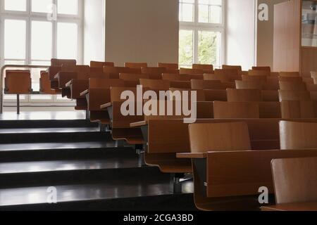 auditorium dell'università con sedie e banche in legno e grandi finestre e scale su un lato. Le sedie sono disposte in file. Foto Stock