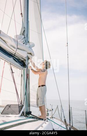 Giovane marinaio hipster regolare vele di yacht bianco contro calmo mare blu e cielo sfondo con copyspace. Foto Stock