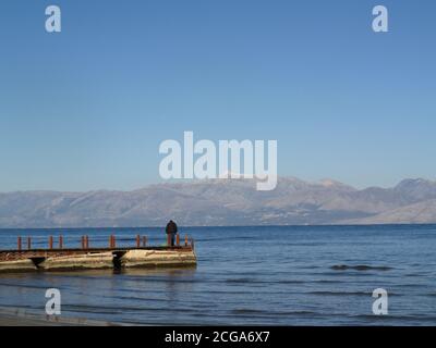 Un uomo si trova da solo sul molo di legno presso GLI alberghi A, Roda Beach Hotel, Resort and Spa, Roda, Corfu, Grecia in inverno Foto Stock