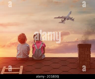 Due bambini che giocano sul tetto della casa e guardano il cielo e sognano di diventare piloti. Foto Stock