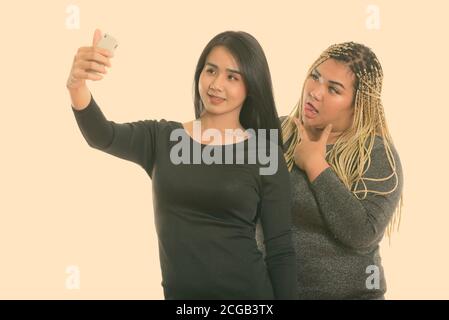 Giovani felici Asian transgender donna e grasso donna asiatica sorridere mentre prendendo selfie foto con telefono cellulare con grasso donna in posa Foto Stock