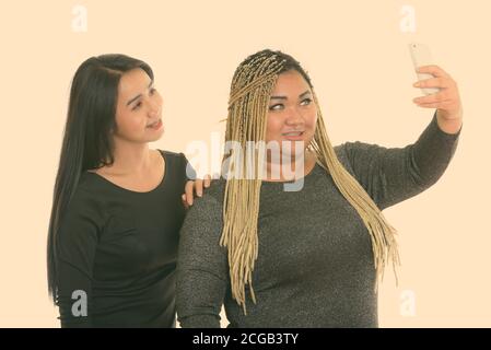 Giovani felici fat donna asiatica e Asian transgender donna sorridente tenendo selfie foto con il telefono cellulare Foto Stock