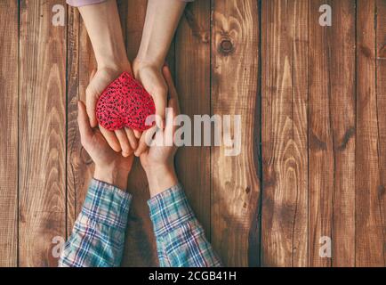Mani di uomo e donna che tengono il cuore rosso su sfondo di legno. Concetto di San Valentino. Vista dall'alto. Primo piano. Foto Stock