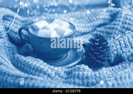 Tazza di caffè, marshmallow, maglione a maglia e ghirlanda a LED su sfondo di legno. Classic Blue trendy colore dell'anno 2020 - immagine Foto Stock