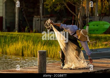 Un pescatore che indossa tute, stivali di plastica e un cappello a secchio sta preparando la sua rete gettata prima di gettarla nella baia di Chesapeake al tramonto. È acceso Foto Stock