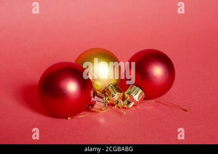 Due palline di Natale rosse e una dorata su sfondo rosso, primo piano Foto Stock