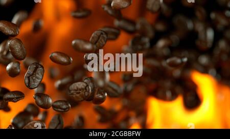 Chicchi di caffè appena tostati che volano nell'aria in fiamme, isolati su sfondo nero Foto Stock