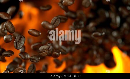 Chicchi di caffè appena tostati che volano nell'aria in fiamme, isolati su sfondo nero Foto Stock