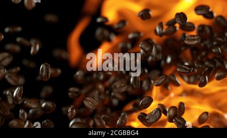 Chicchi di caffè appena tostati che volano nell'aria in fiamme, isolati su sfondo nero Foto Stock