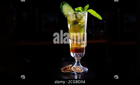 Un cocktail verde o una limonata con cetriolo in un alto vetro si erge sul banco di un bar scuro. Foto Stock