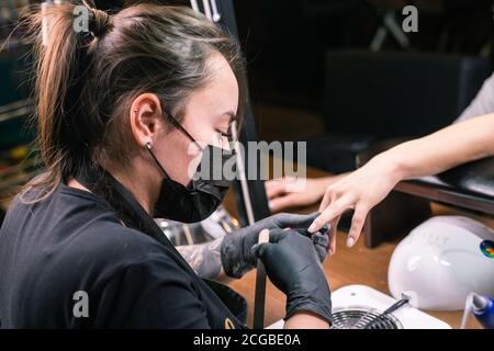 Il padrone femminile usa una macchina elettrica per rimuovere lo smalto del chiodo durante il manicure nel salone. Primo piano manicure hardware. Concetto di cura delle mani Foto Stock