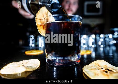 Un cocktail con whisky o cognac o Cola in un bicchiere di highball si trova al bancone di un bar scuro. Foto Stock