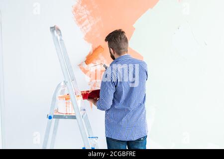 Uomo felice pittura parete interna con rullo di vernice in nuova casa. Ragazzo con rullo che applica la vernice su una parete. Vista posteriore. Foto Stock