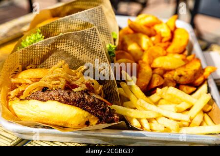 Hamburger, patate, ketchup e tazze di birra sul tavolo di un caffè di strada. Foto Stock