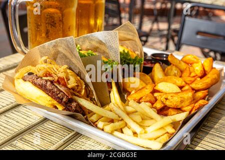 Hamburger, patate, ketchup e tazze di birra sul tavolo di un caffè di strada. Foto Stock