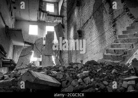 Immagine in bianco e nero. Edificio in cemento distrutto all'interno con un mucchio di detriti di costruzione in primo piano e grandi lastre di cemento appese a reba Foto Stock