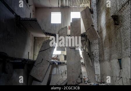 Edificio in cemento distrutto all'interno con un mucchio di detriti di costruzione in primo piano e grandi lastre di cemento appese sulla barra contro il muro posteriore Foto Stock