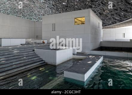 Un'immagine interna del Louvre Abu Dhabi che include un'area salotto al bordo dell'acqua, il suo tetto ad alta tecnologia e le pareti bianche della facciata dei suoi vari spazi espositivi. Aperto a novembre 2017. Foto Stock