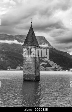 Il vecchio campanile della chiesa di Curon Venosta si immerse in bianco e nero nel lago di Resia, in Alto Adige, contro un cielo drammatico Foto Stock