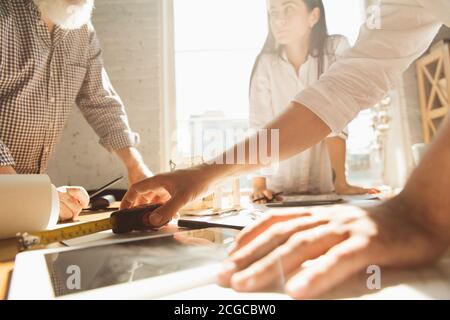 Mani di architetto-ingegnere e giovane coppia durante la presentazione della futura casa. Tabella vista laterale con documenti, blueprint. Primo concetto di casa, industriale, edilizia. Passaggio a un nuovo live place. Foto Stock