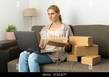 giovane donna piccolo imprenditore in linea di affari seduto sul divano e preparare il pacchetto per la spedizione sul laptop a casa. imprenditore sme Foto Stock
