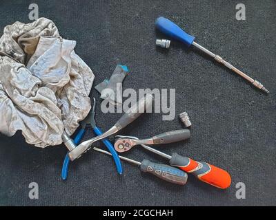 Strumenti di lavoro. Cacciaviti, pinze e varie ispezioni giacciono su uno sfondo nero accanto a uno straccio sporco nel garage Foto Stock