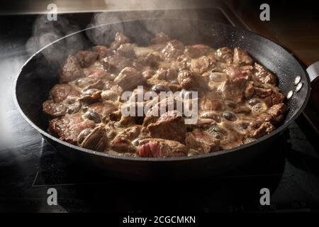 Sfrigolatura e cottura a vapore di manzo in una padella per goulash o stufato, cottura a casa, fuoco selezionato, profondità di campo ridotta, Foto Stock