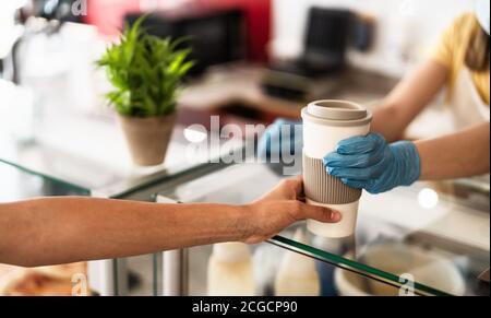 Il proprietario del bar lavora solo con gli ordini di take away durante l'epidemia di virus corona - giovane donna che indossa la maschera chirurgica del viso che dà caffè al cliente Foto Stock