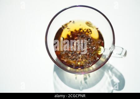 Tazza di vetro trasparente con tè al fiore nero. Vista dall'alto su un tavolo bianco e soleggiato con ombra. Foto Stock